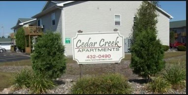 A sign for Cedar Creek Apartments is in front of a building.