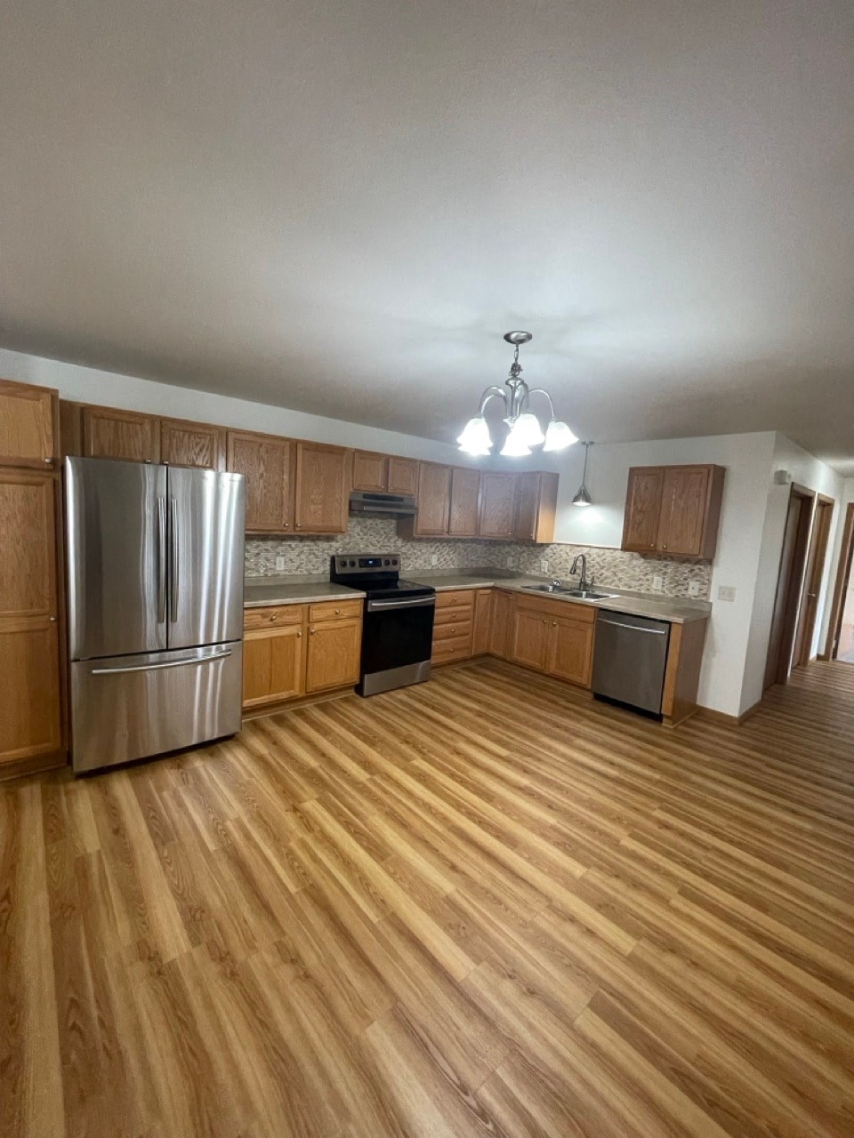 an empty kitchen with wooden floors and stainless steel appliances