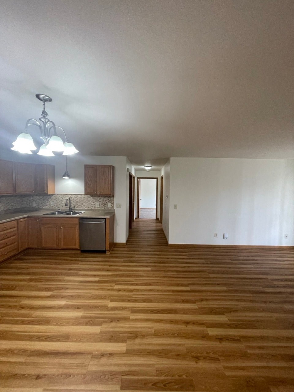 an empty living room with wooden floors and a kitchen