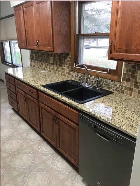 A kitchen with a black sink and wooden cabinets.