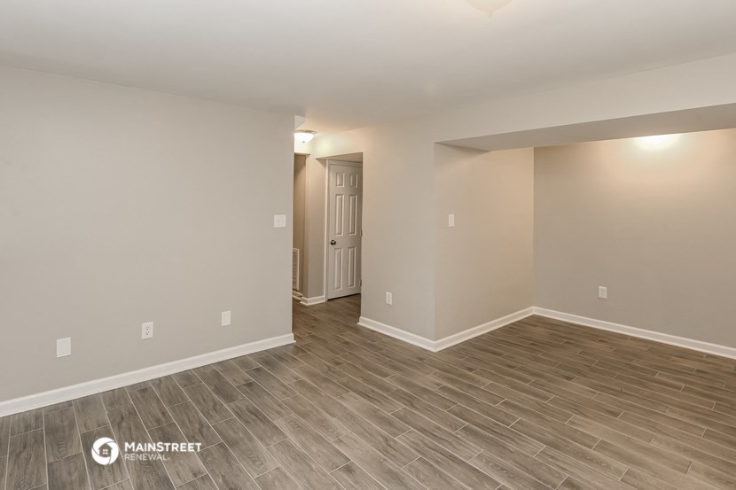 the spacious living room with wood flooring and a door to the hallway
