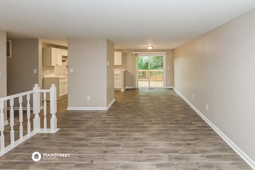 a large empty living room with a staircase and a kitchen