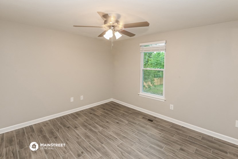 the spacious living room with wood flooring and a ceiling fan