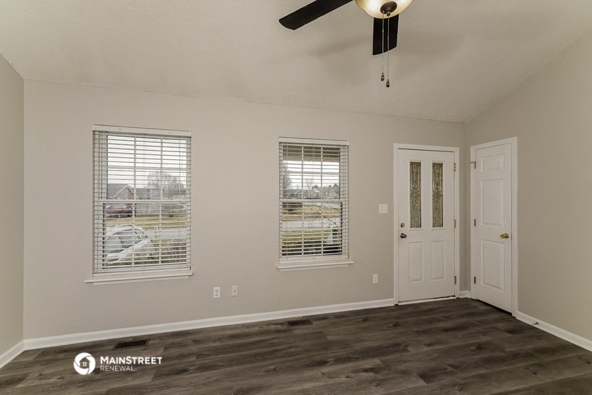 the spacious living room of an empty home with a door and windows