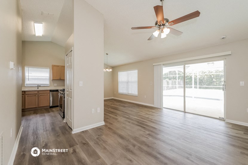 an empty living room with a ceiling fan and a kitchen