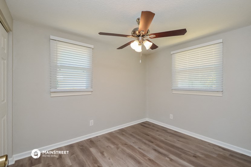 the spacious living room with a ceiling fan and two windows