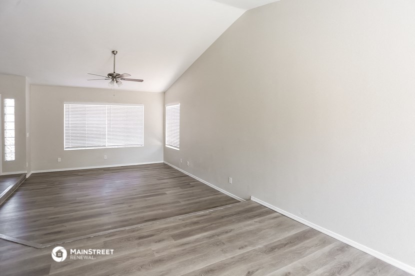 the spacious living room with wood flooring and a ceiling fan