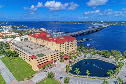 A large building with a red roof is surrounded by a pool and palm trees.