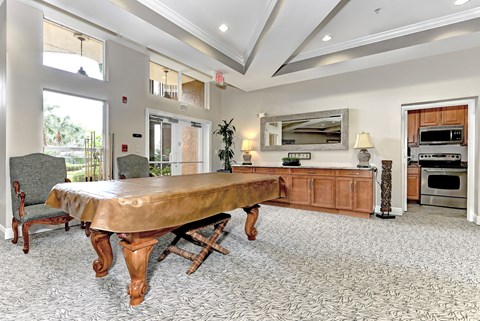 A large dining table with a wooden top and turned legs sits in a spacious room with a kitchen in the background.