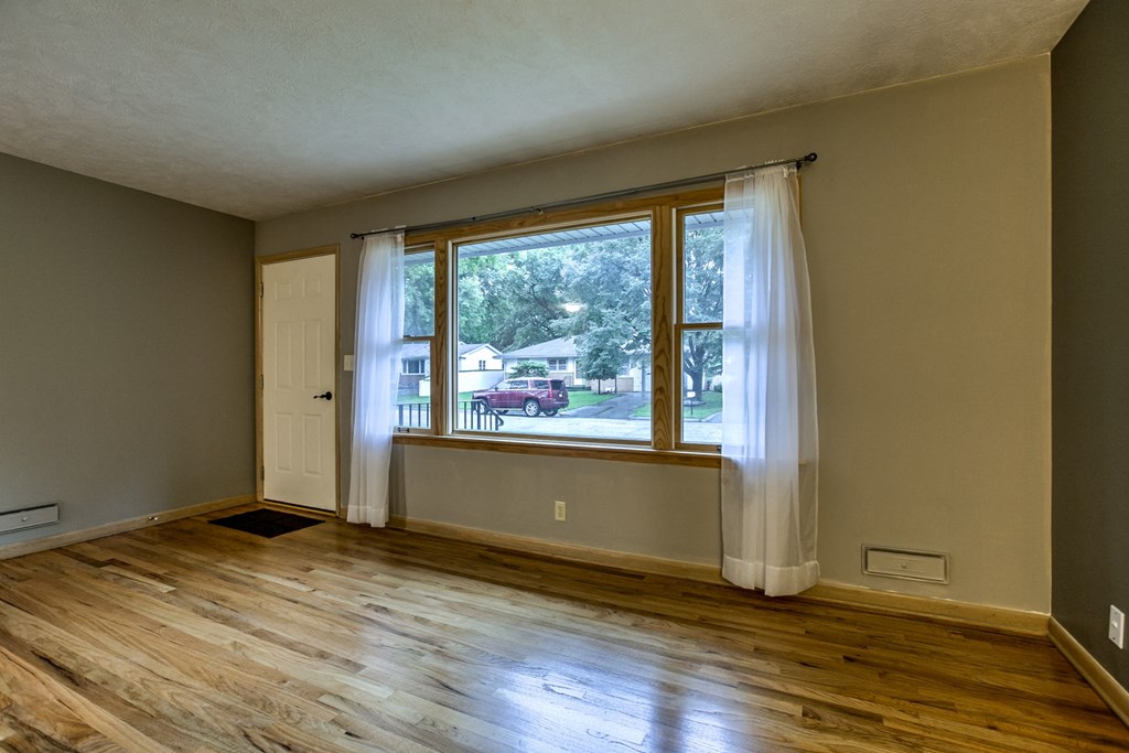 an empty living room with wooden floors and a large window