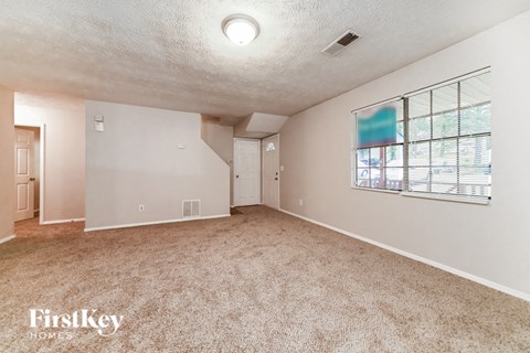 A spacious room with a carpeted floor and a window with blinds.