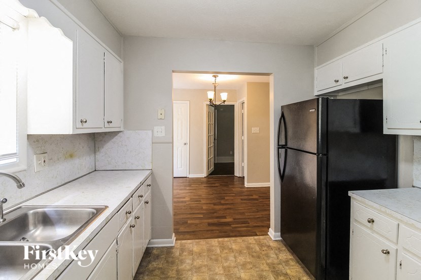 a kitchen with white cabinets and stainless steel appliances and a hallway with a black refrigerator