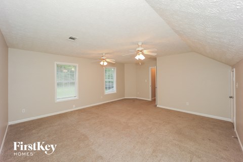 A spacious room with a ceiling fan and two windows.