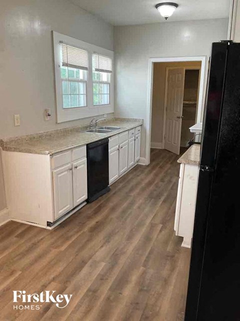 A kitchen with a black refrigerator and wooden floors.