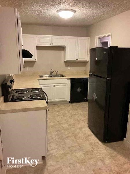 A black refrigerator is in a kitchen with white cabinets.