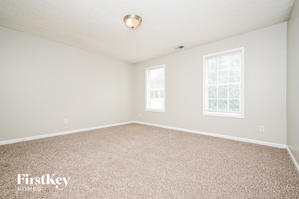 A room with a carpeted floor and two windows.