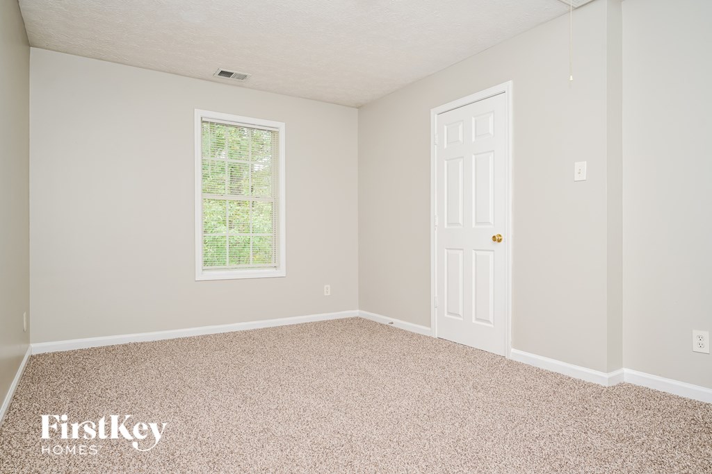 A room with a carpeted floor, a door, and a window with a view of trees.