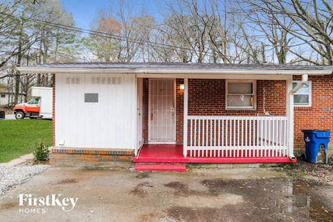 the front porch of a small brick home with a white door and a red porch