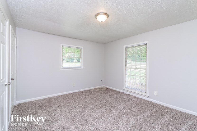 A room with a carpeted floor, two windows, and a door.