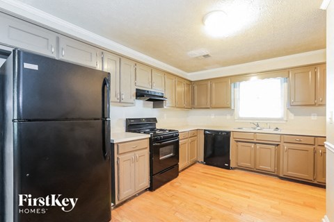 A black refrigerator with the words "FirstKey Homes" on it is in a kitchen with wooden floors and cabinets.