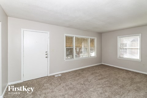 A room with a carpeted floor, a white door, and a window with blinds.