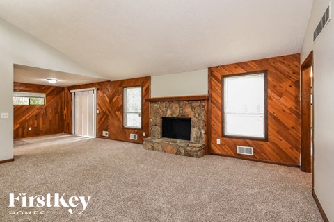an empty living room with a stone fireplace and wooden walls