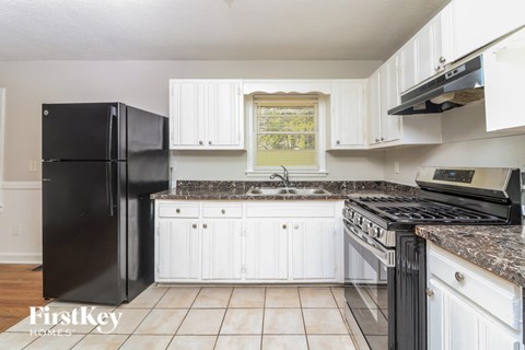 A black refrigerator sits in a kitchen with white cabinets and a granite countertop.