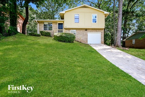 A yellow house with a white garage door is surrounded by green grass and trees.