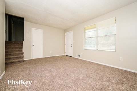 A spacious room with a carpeted floor and a window with blinds.