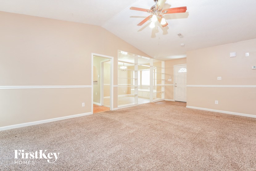 a spacious living room with carpet and a ceiling fan