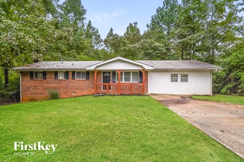 A house with a red door and a porch is surrounded by greenery.