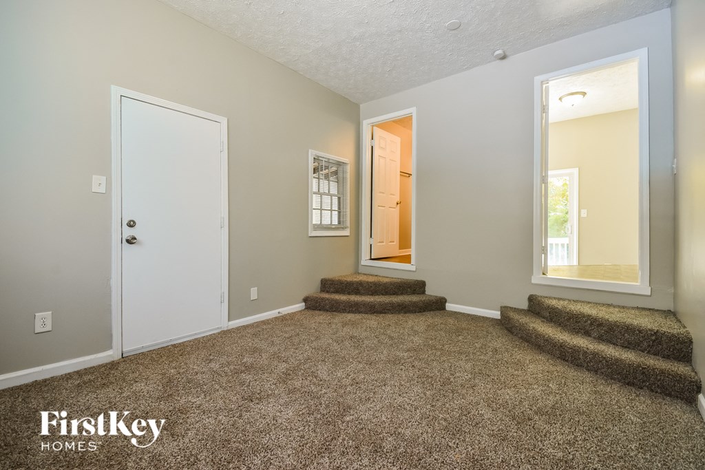 a living room with carpeted stairs and a door to a hallway