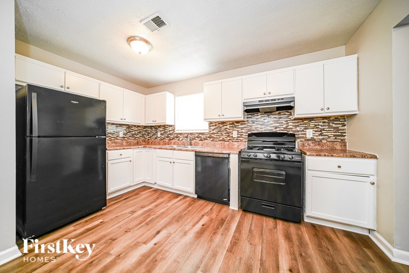 A kitchen with a black fridge, black oven and white cabinets.