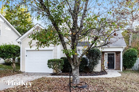 A tree stands in front of a house with a garage door.