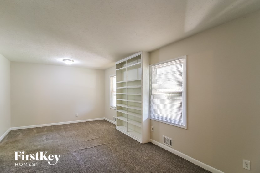 A room with a window covered by white blinds and a carpet on the floor.