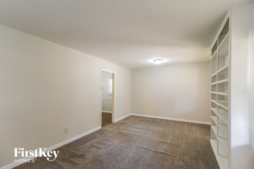 A spacious room with a carpeted floor and a staircase on the right side.