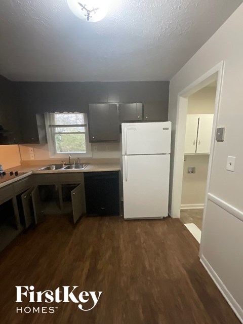 A kitchen with a white fridge and wooden floors.