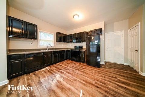 A kitchen with black cabinets and a wooden floor.