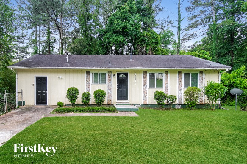 A house with a black door and a white front door is surrounded by greenery.