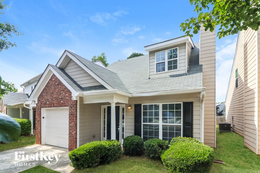 A house with a brick chimney and a white garage door is for sale.