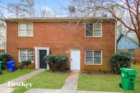 the front of a brick house with a white door and green trash cans