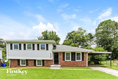 a white and brick house with a green lawn and a blue sky