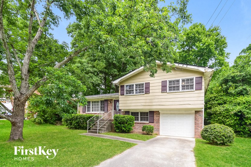 A house with a garage is surrounded by green trees.