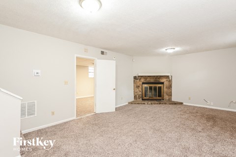 A spacious living room with a fireplace and carpeted floor.
