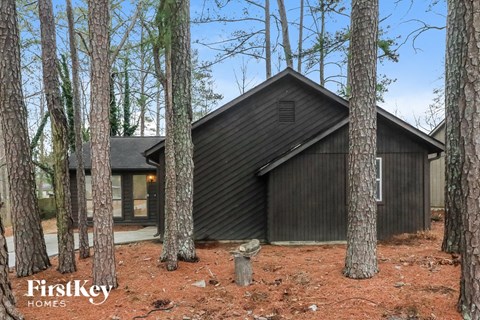 A black house with a triangular roof is nestled among tall trees.