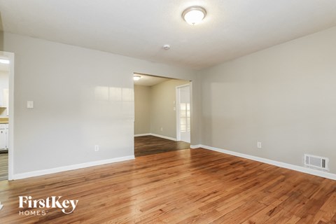 A spacious room with wooden floors and white walls, with a doorway leading to another room.