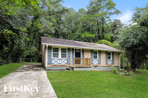A small house with a porch is surrounded by greenery.