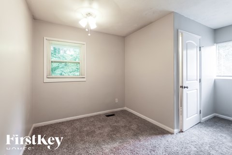 A room with a carpeted floor, a window with a view of trees, and a door leading to another room.