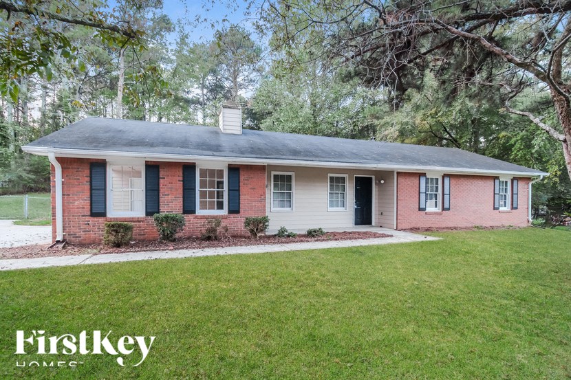 a small brick house with black shutters and a green lawn