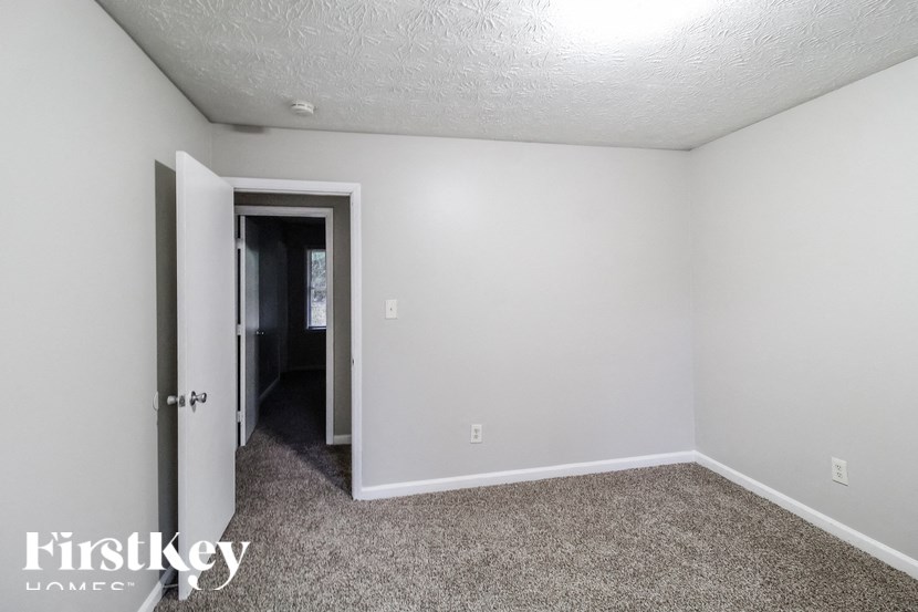 a bedroom with white walls and carpet and a door to a hallway